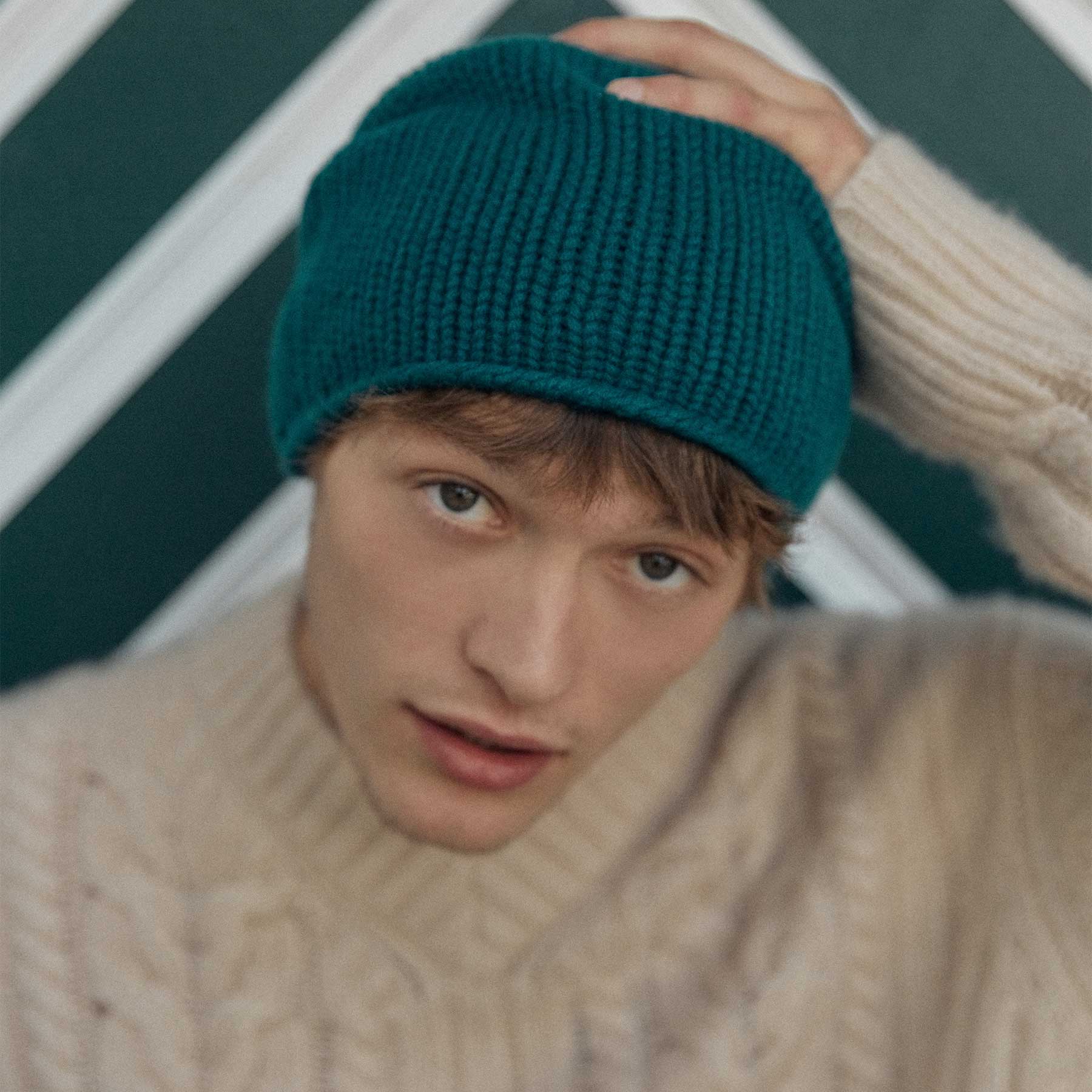Grüner, gestrickter Beanie auf einem gestreiften Hintergrund